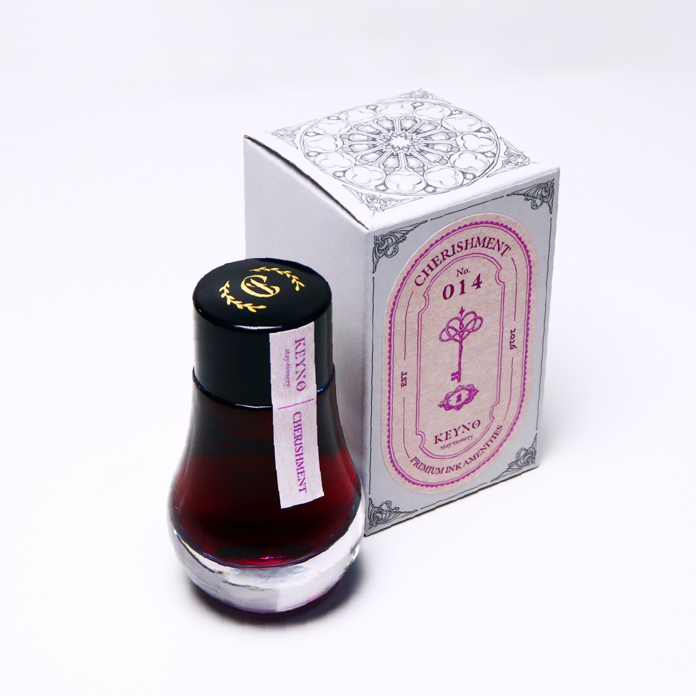 Bottle of pink ink with a black cap next to its packaging on a white background