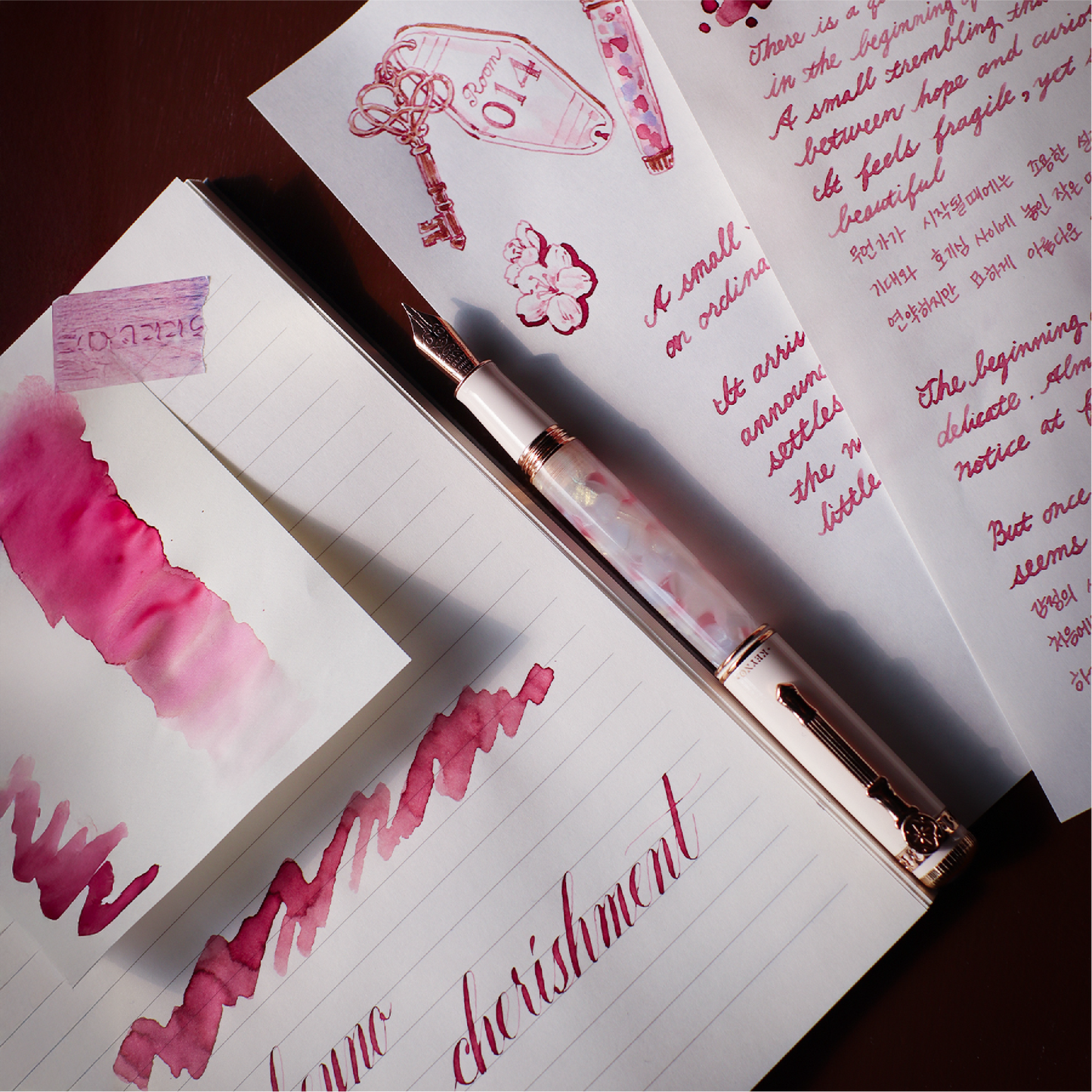 Ink swatches and a pen on a notebook with pink calligraphy