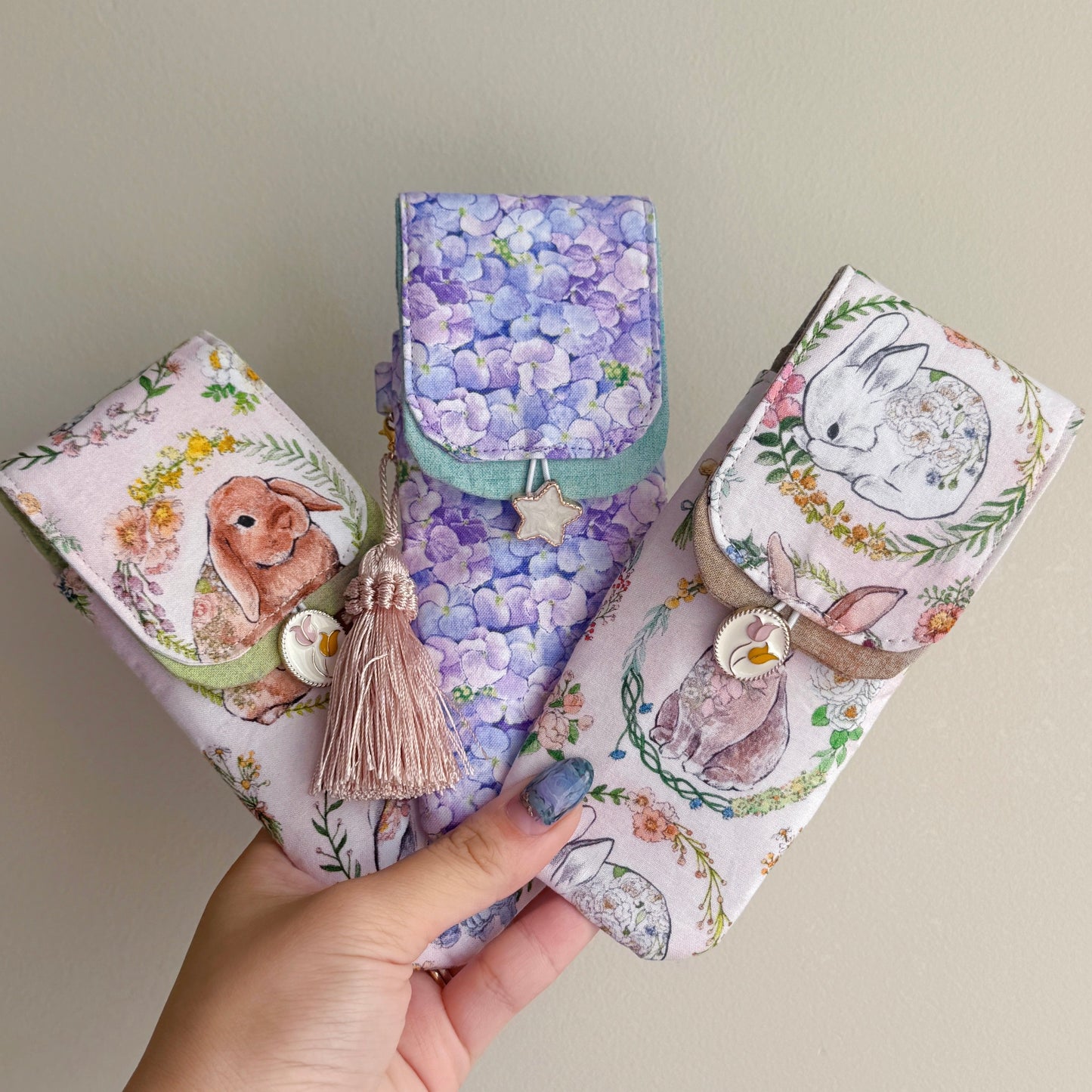 Three handmade fabric pen pouches with rabbit designs held by a hand against a neutral background