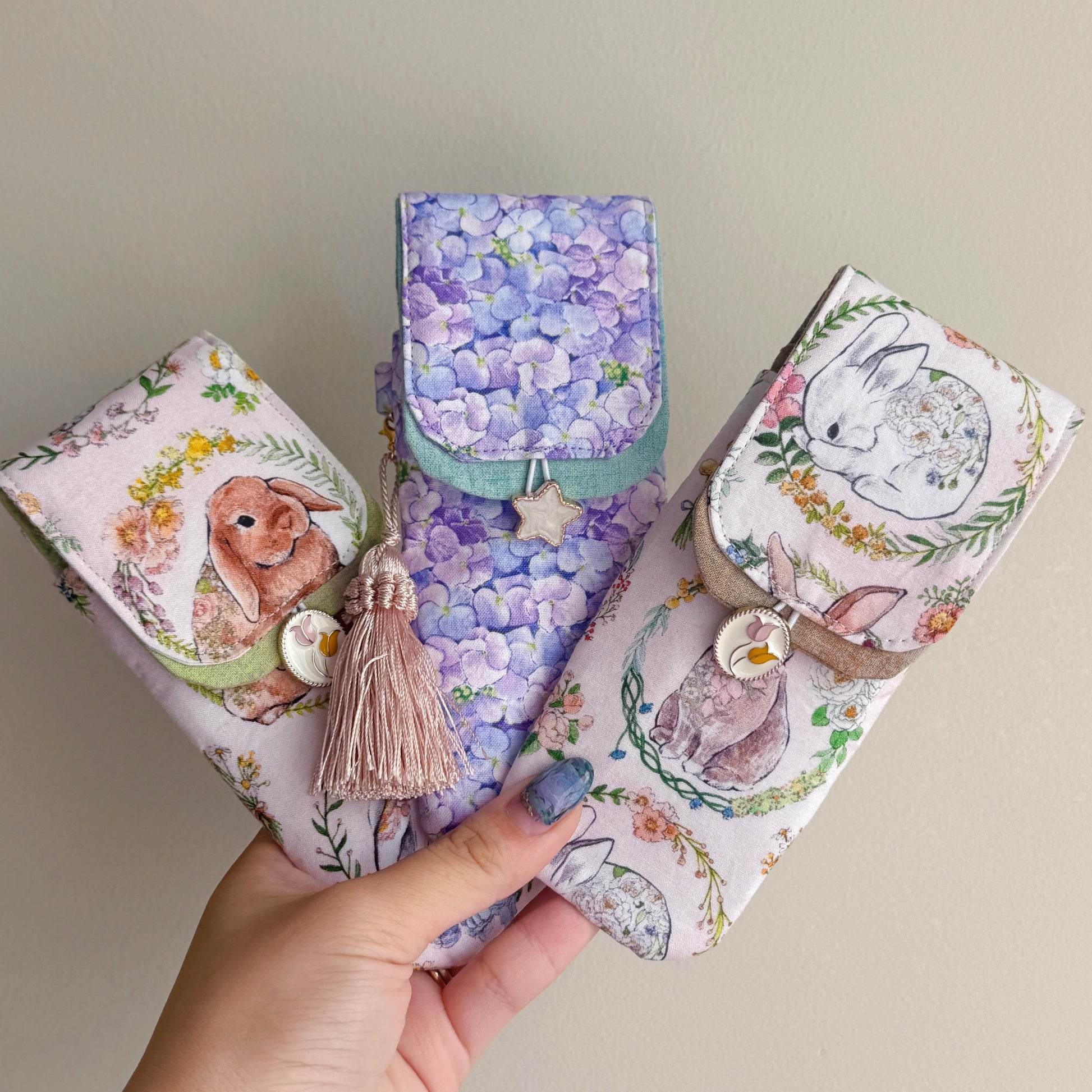 Three handmade fabric pen pouches with rabbit designs held by a hand against a neutral background