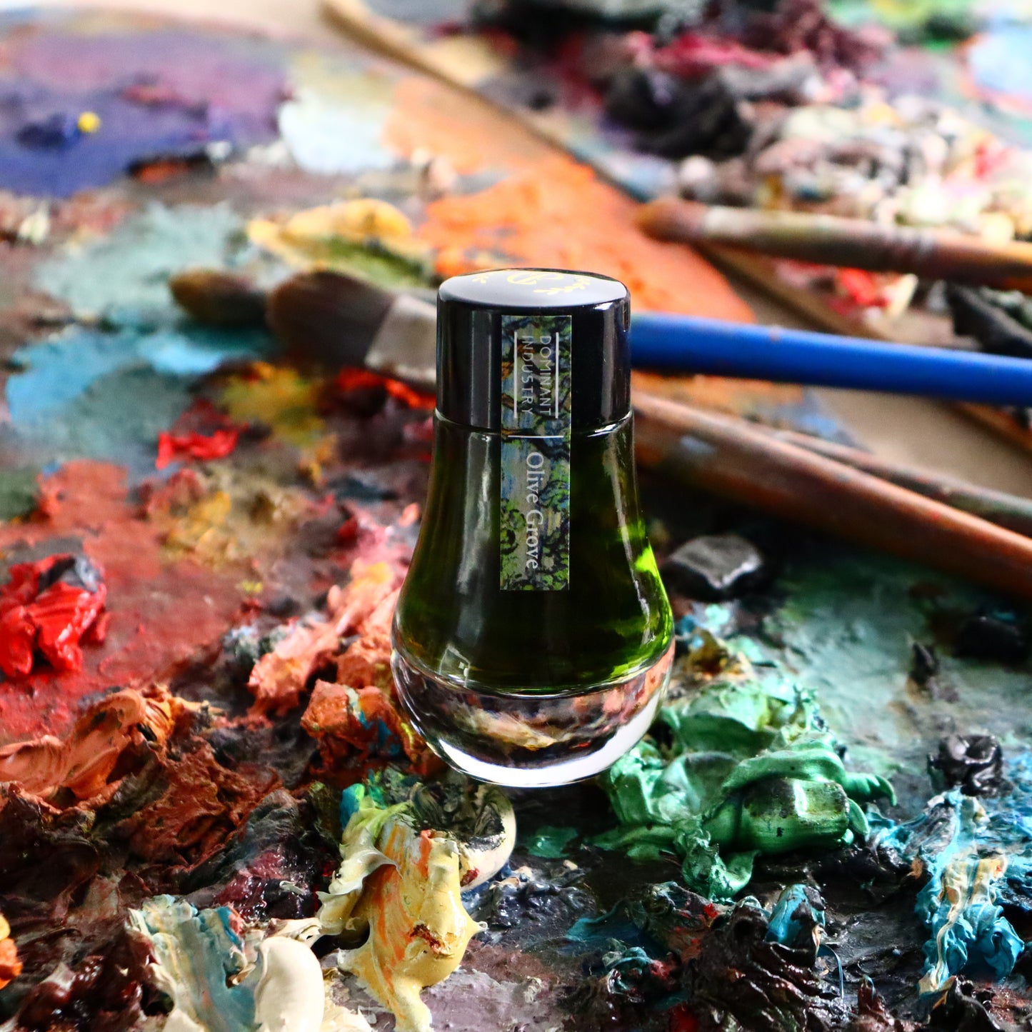 Dominant Industry Olive Grove ink bottle on a paint palette with brushes
