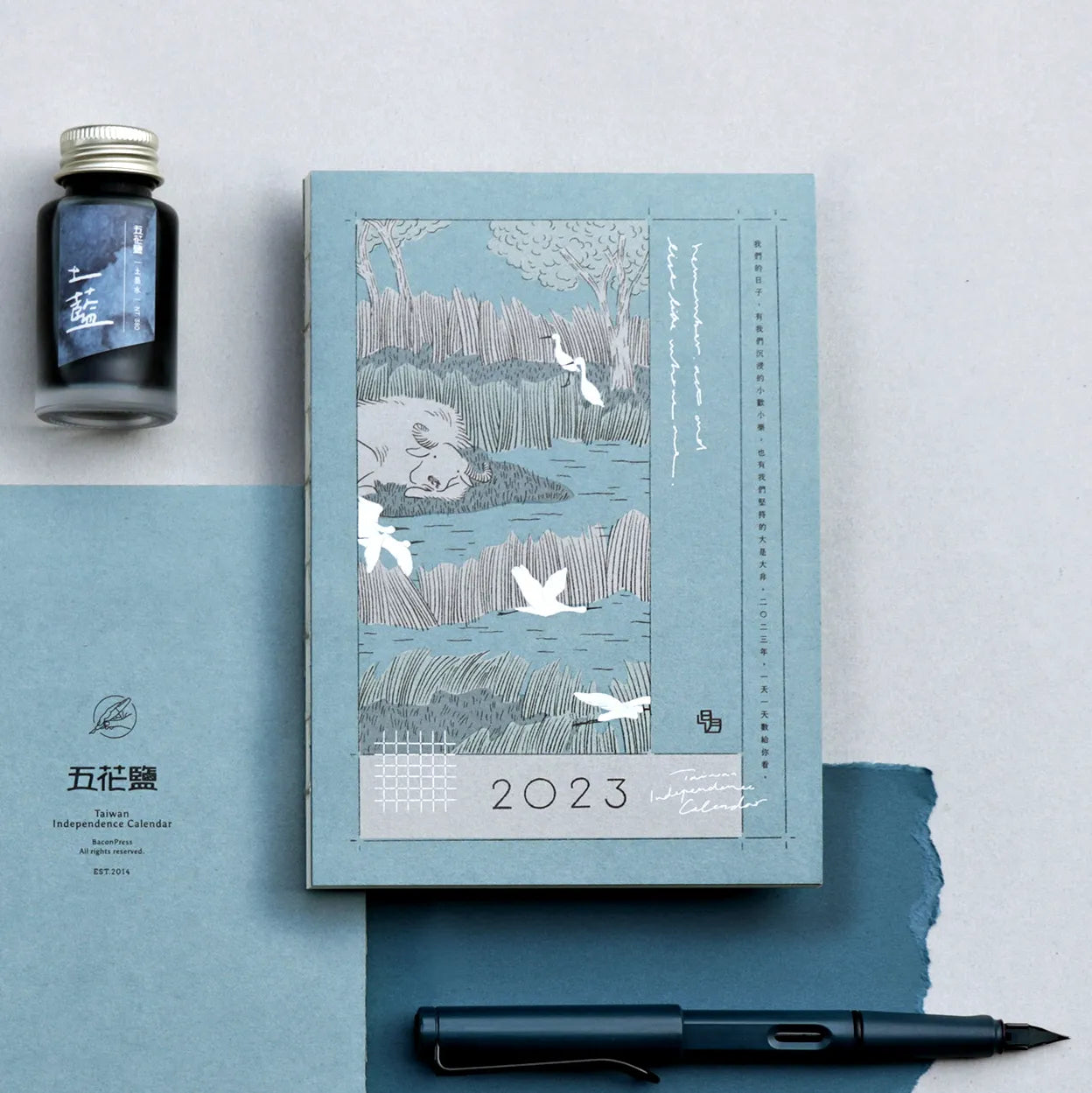 2023 calendar with artistic design, ink bottle, and pen on a light blue background