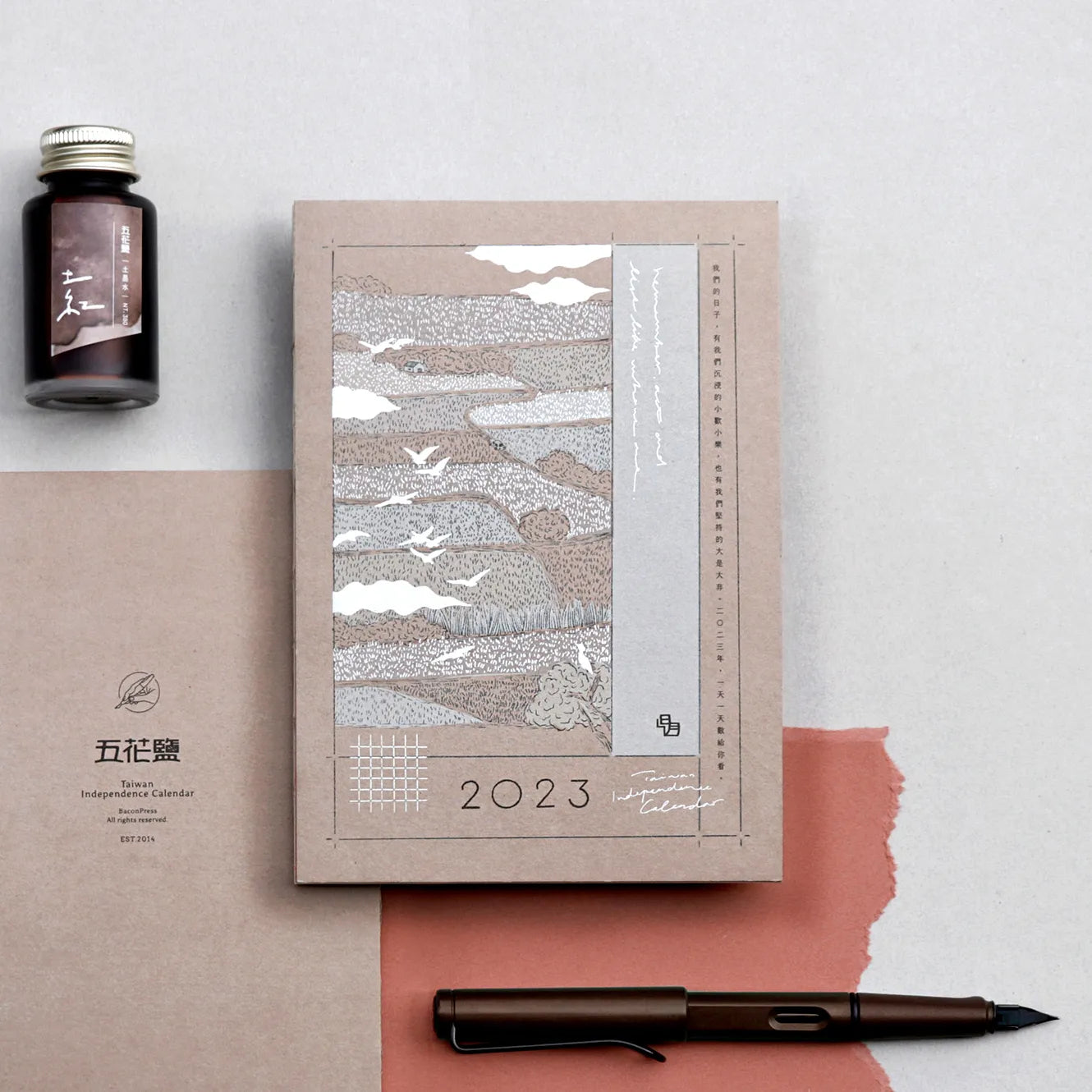 2023 calendar with artistic design, pen, and ink bottle on a light background