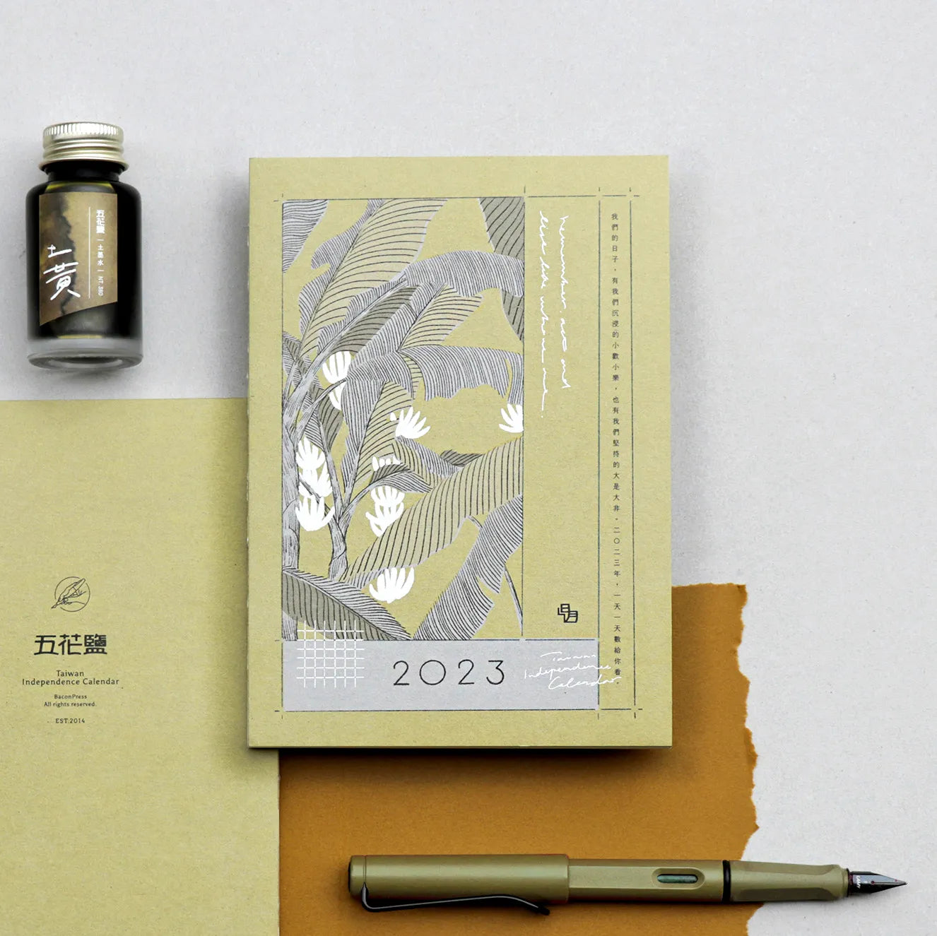 2023 calendar with leaf design, ink bottle, and fountain pen on a light gray background