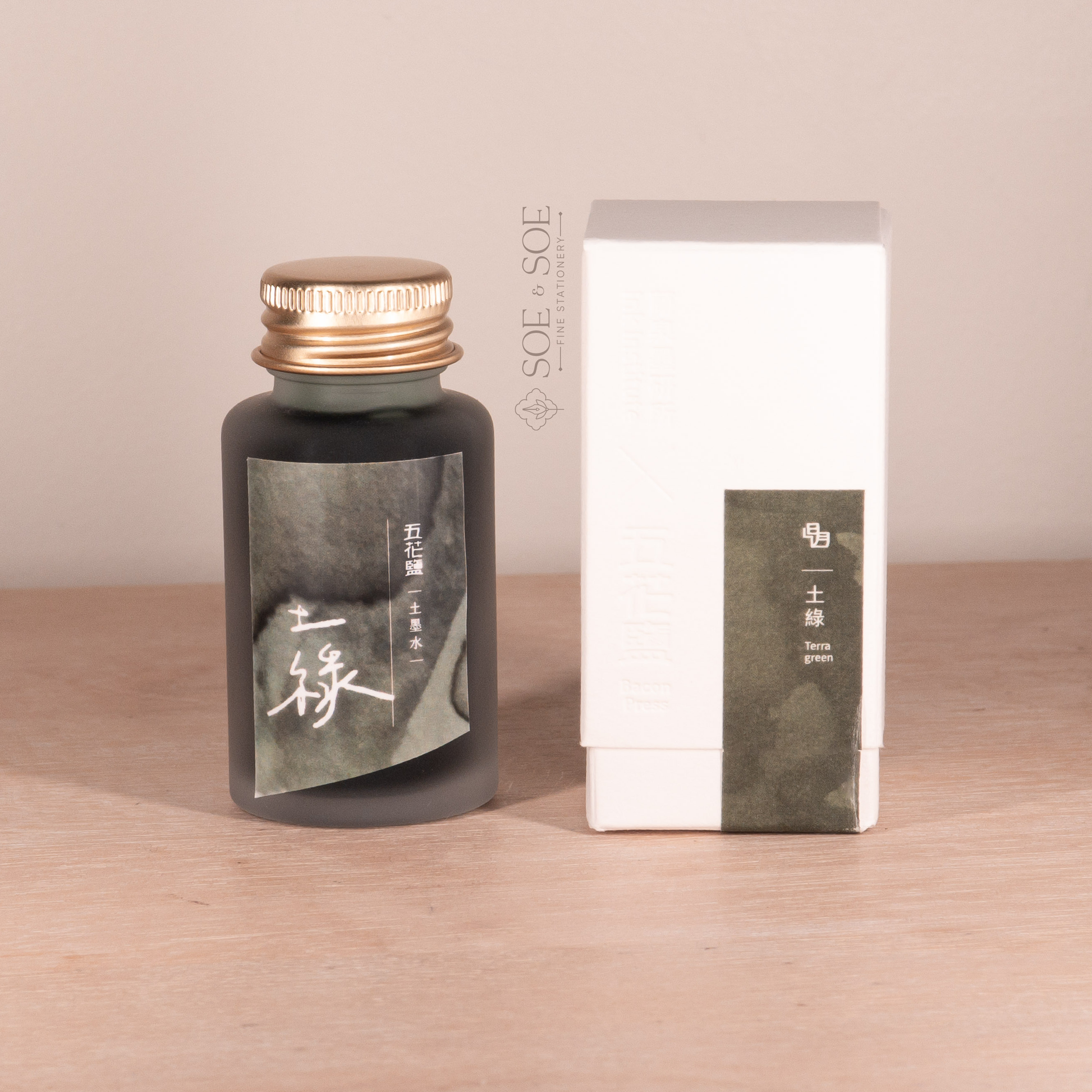 Fountain pen ink bottle and packaging with 'SOE & SOE' branding on a wooden surface.