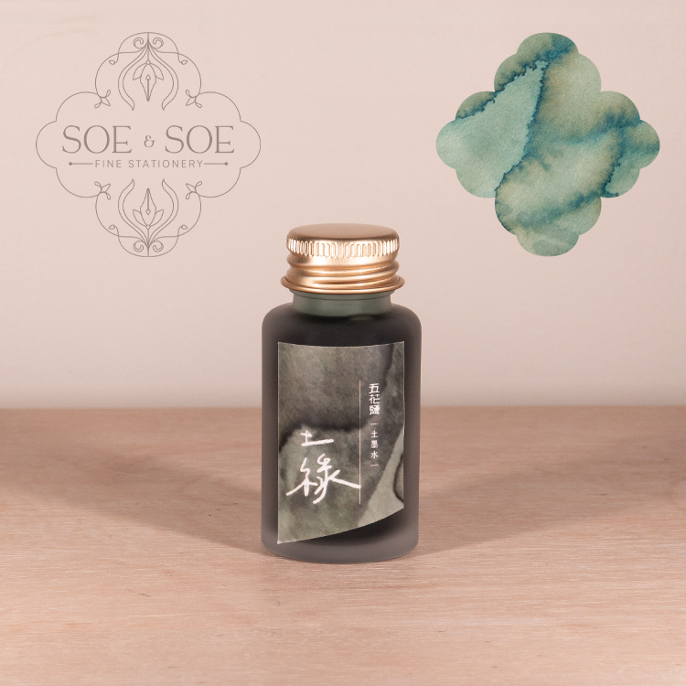 Fountain pen ink bottle with gold cap on a wooden surface, SOE & SOE brand visible
