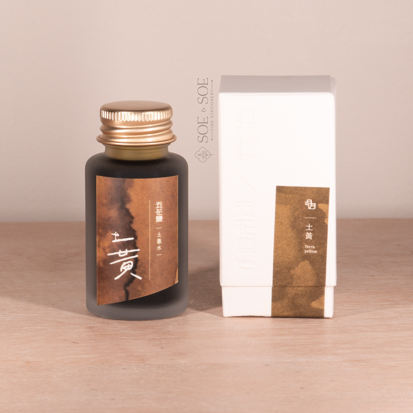 Ink bottle and packaging with gold cap and brown label on a beige background
