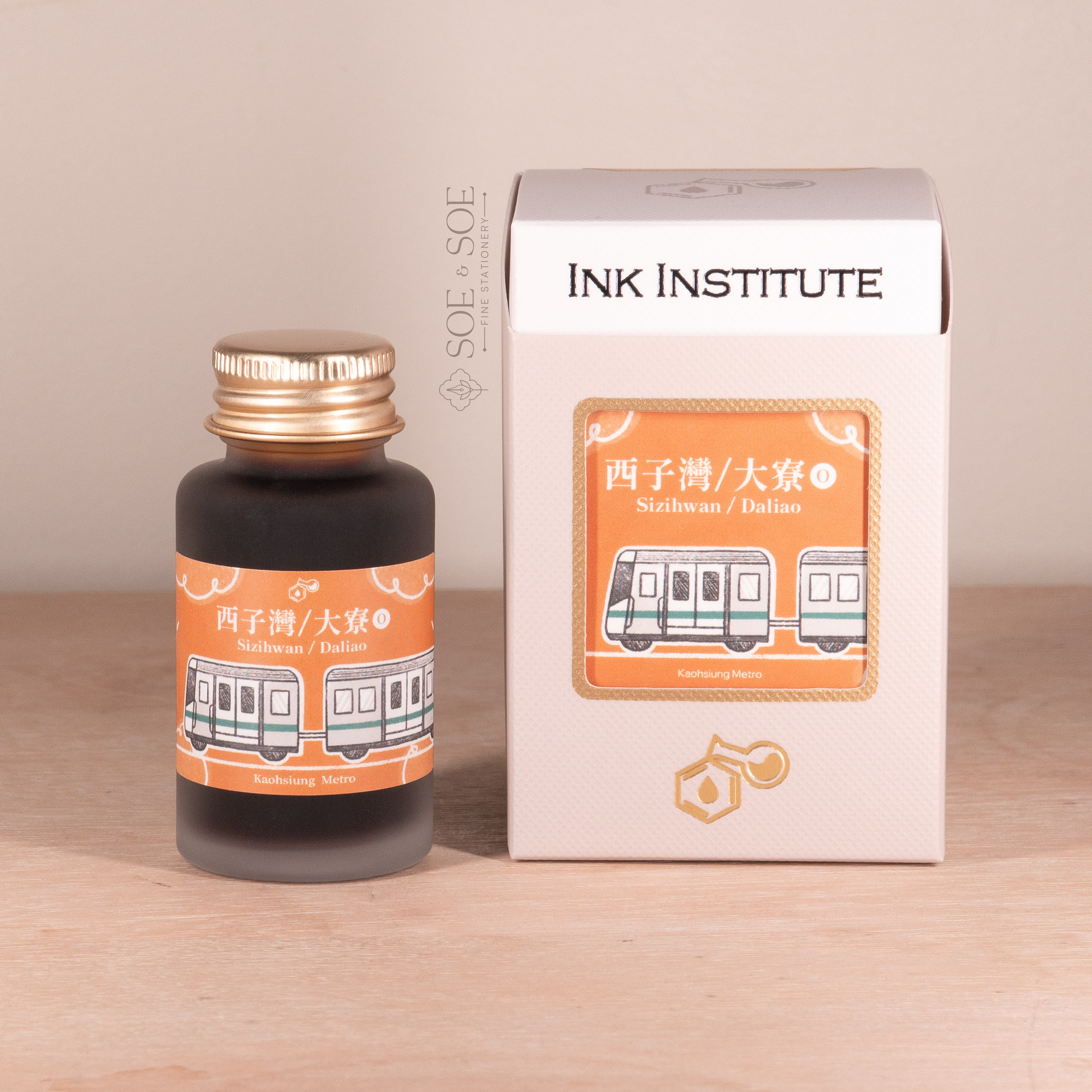 Orange ink bottle and packaging with 'Ink Institute' branding on a wooden surface.