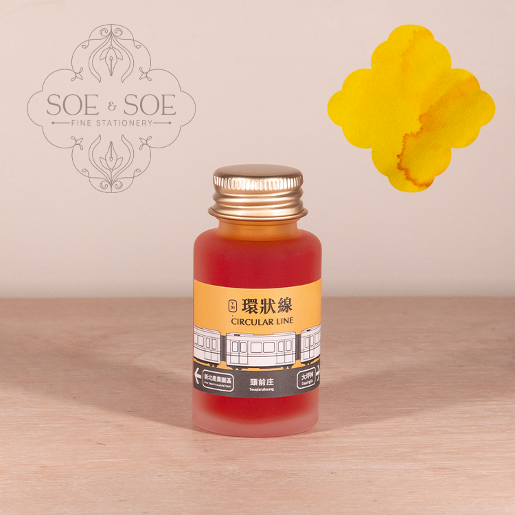 Bottle of yellow ink with a gold cap on a wooden surface, featuring the 'SOE & SOE' brand.