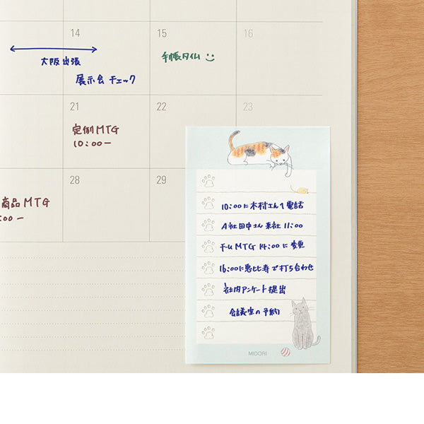 Calendar with a cat illustration stickyy note and Japanese text on a wooden surface