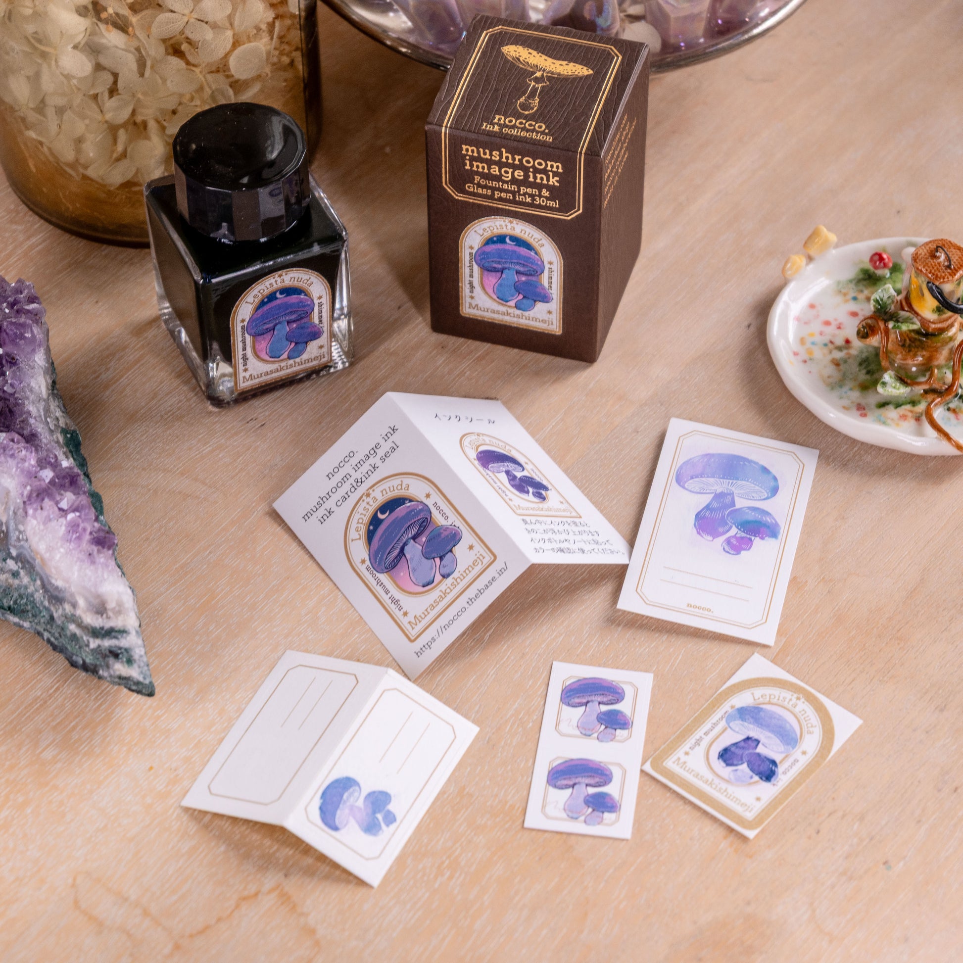 Mushroom-themed cards and ink bottle on a wooden surface with decorative items.
