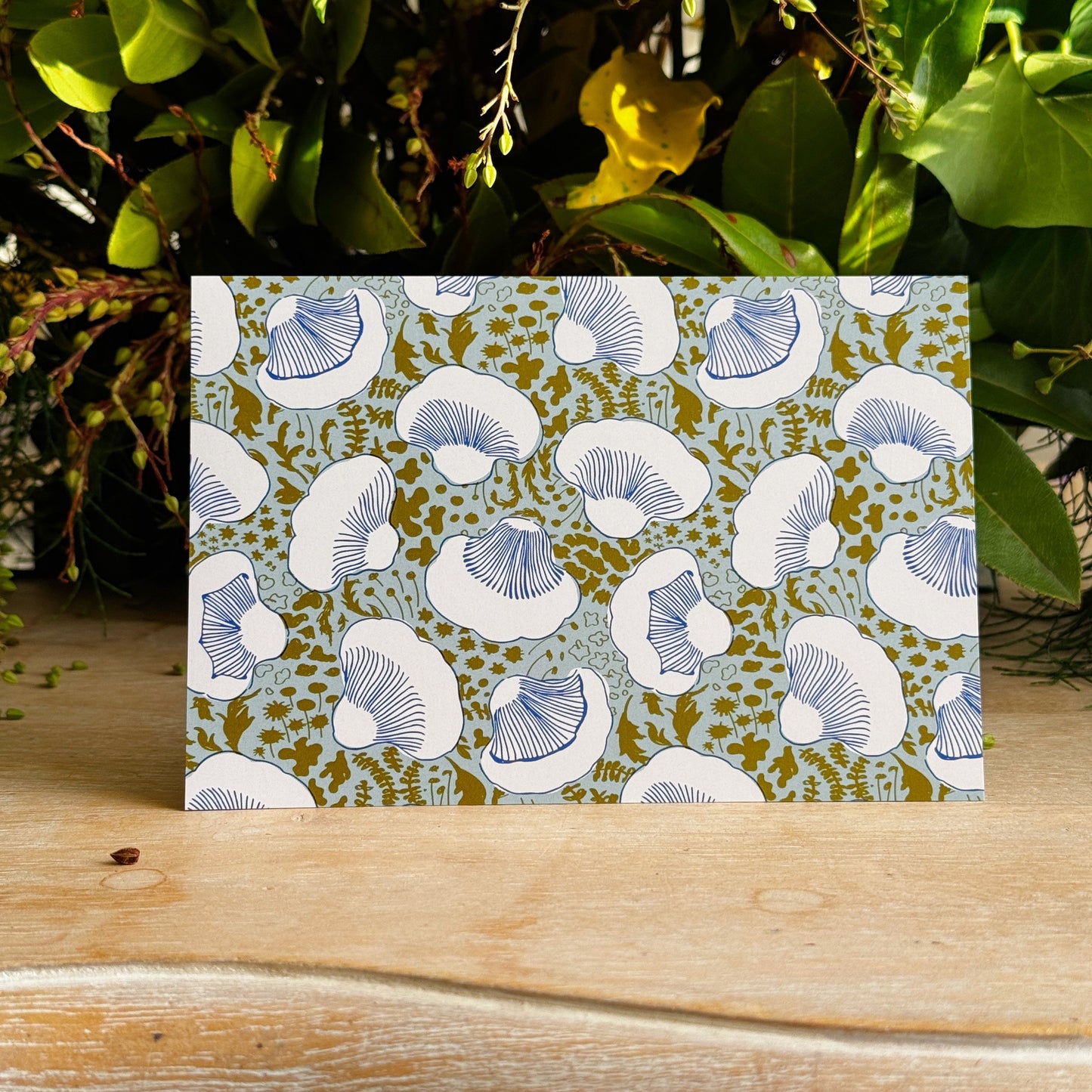 Card with mushroom pattern on a wooden surface with greenery in the background